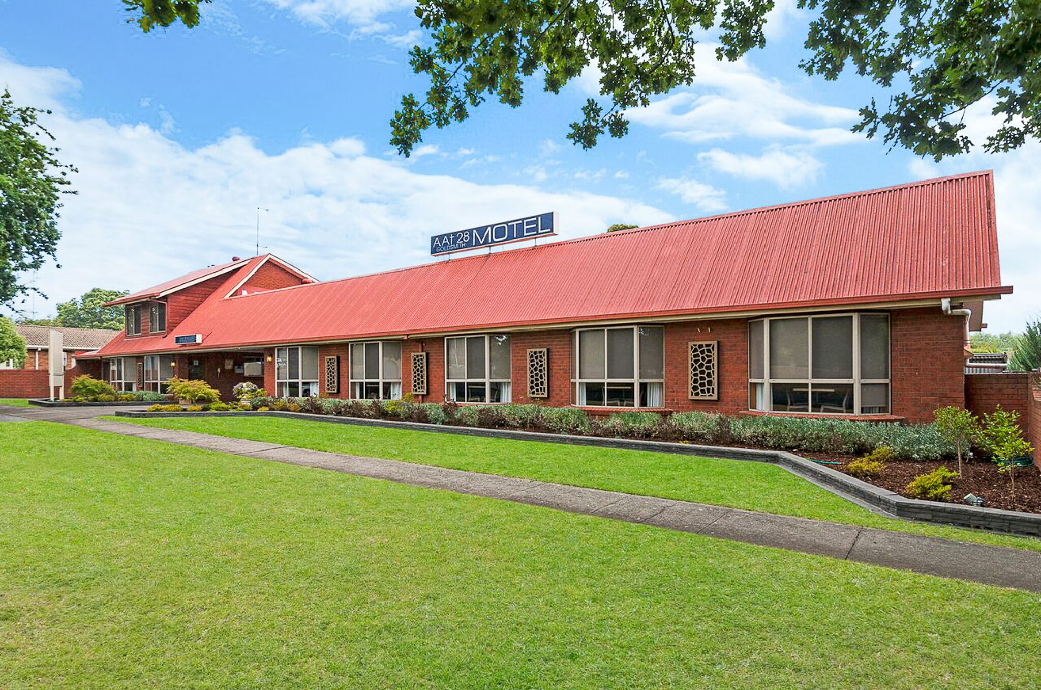 A motel with a red roof and brick exterior, featuring a signboard and a well-maintained lawn.