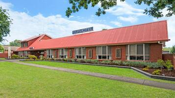A motel with a red roof and brick exterior, featuring a signboard and a well-maintained lawn.