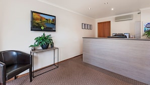 A reception area with a reception desk, a black leather chair, a potted plant, and a framed picture on the wall.