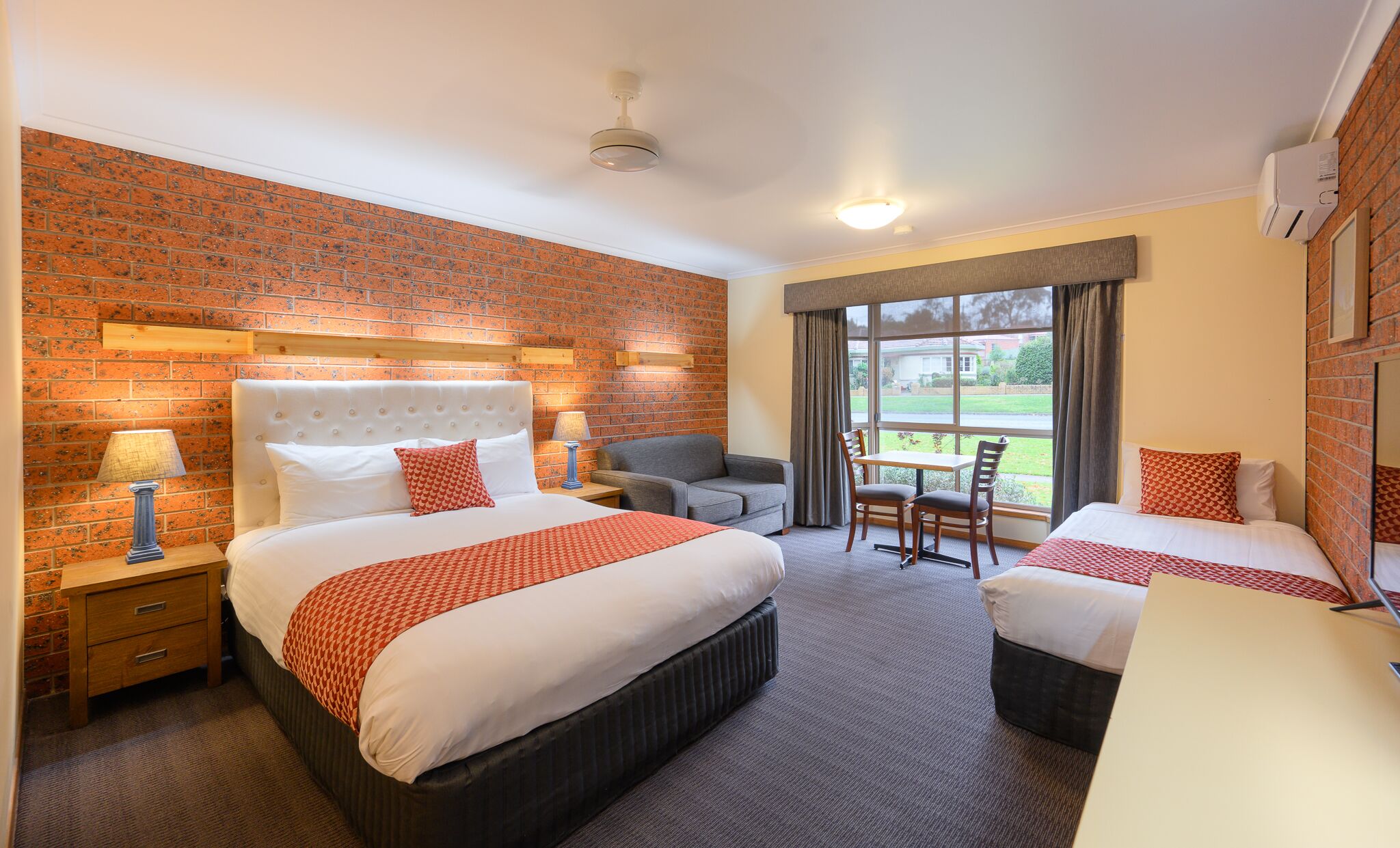 A hotel room with two beds, a brick wall, a large window, and a view of the outdoors.