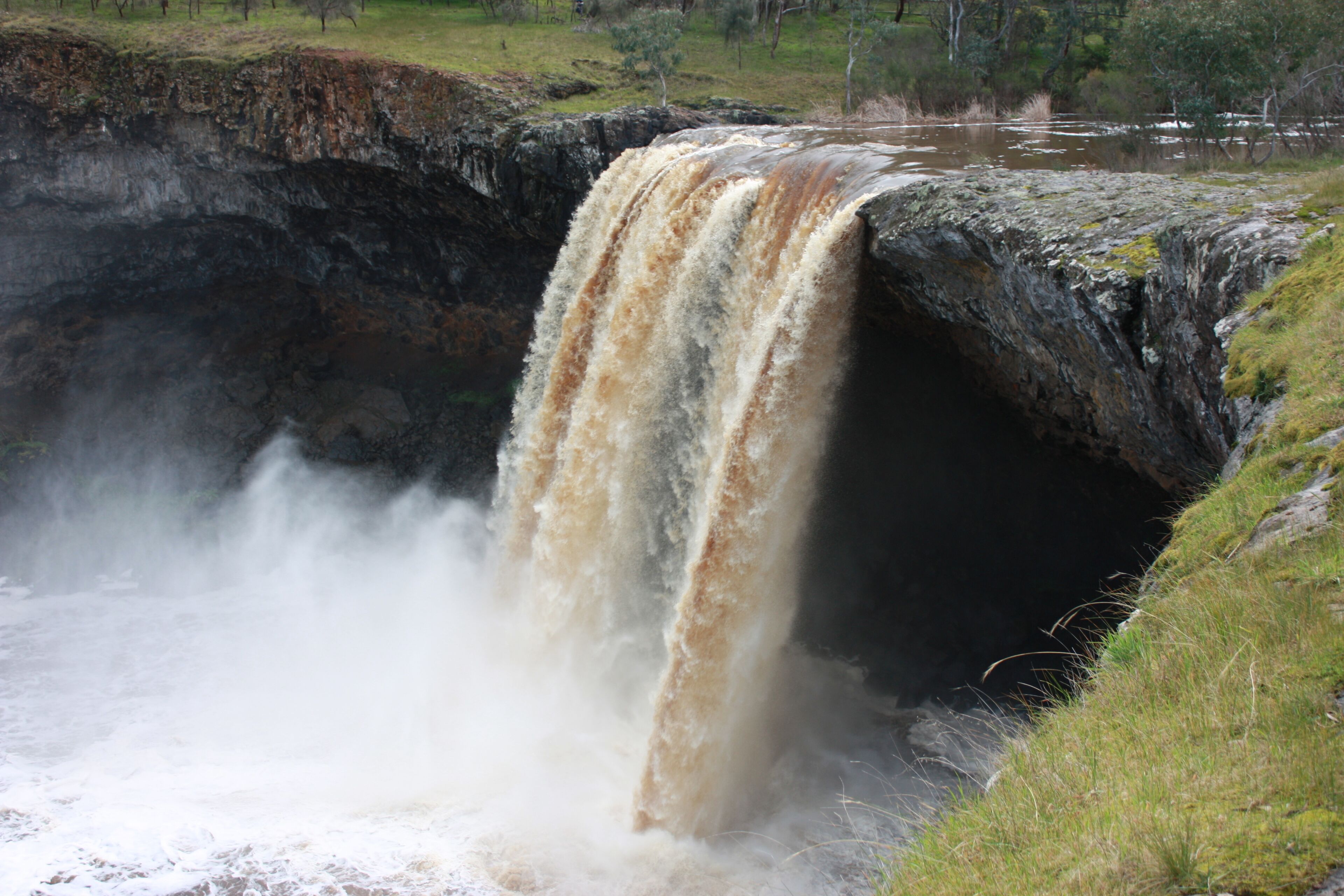 A waterfall cascading into a rocky gorge with grassy banks.