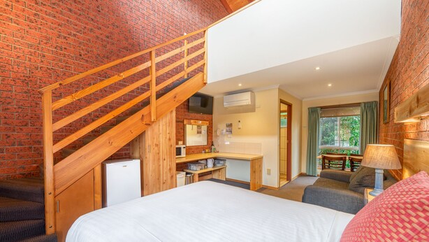 A bedroom with a bed, a desk, a chair, and a staircase.