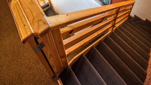 A wooden staircase leading to a bedroom with a brick wall, a window with curtains, and a bed with a pillow.