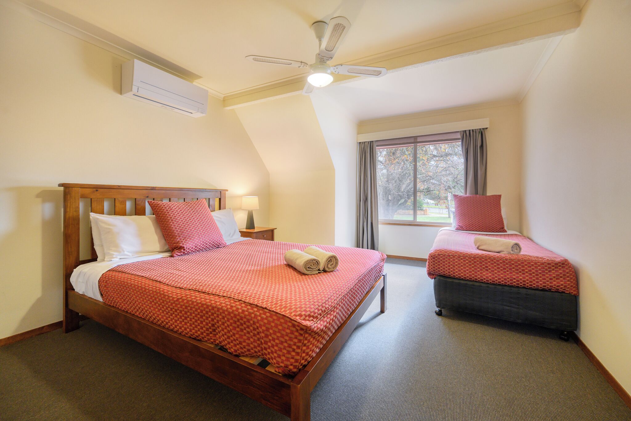 A bedroom with two beds, a ceiling fan, an air conditioning unit, and a window with curtains.