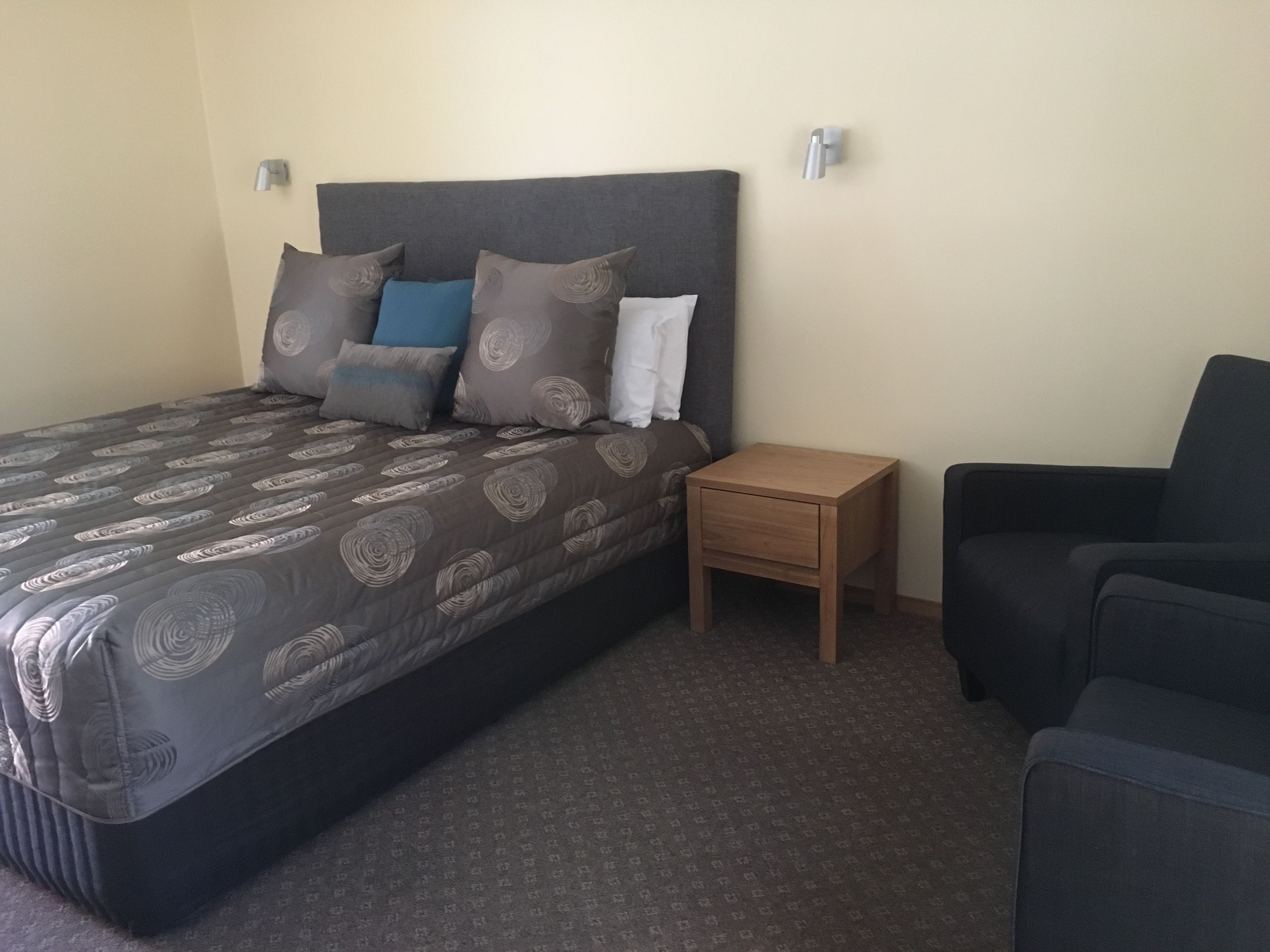 A neatly arranged bedroom with a bed, a nightstand, and a chair.