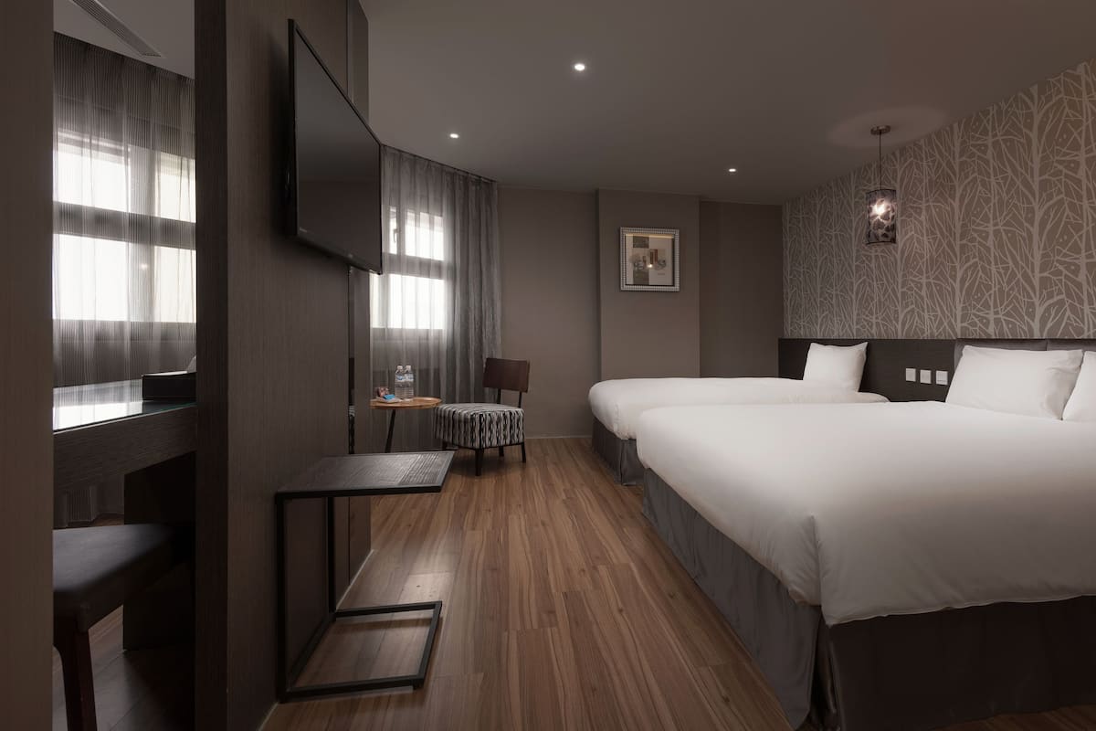 A hotel room with a large bed, a desk, a chair, and a TV.