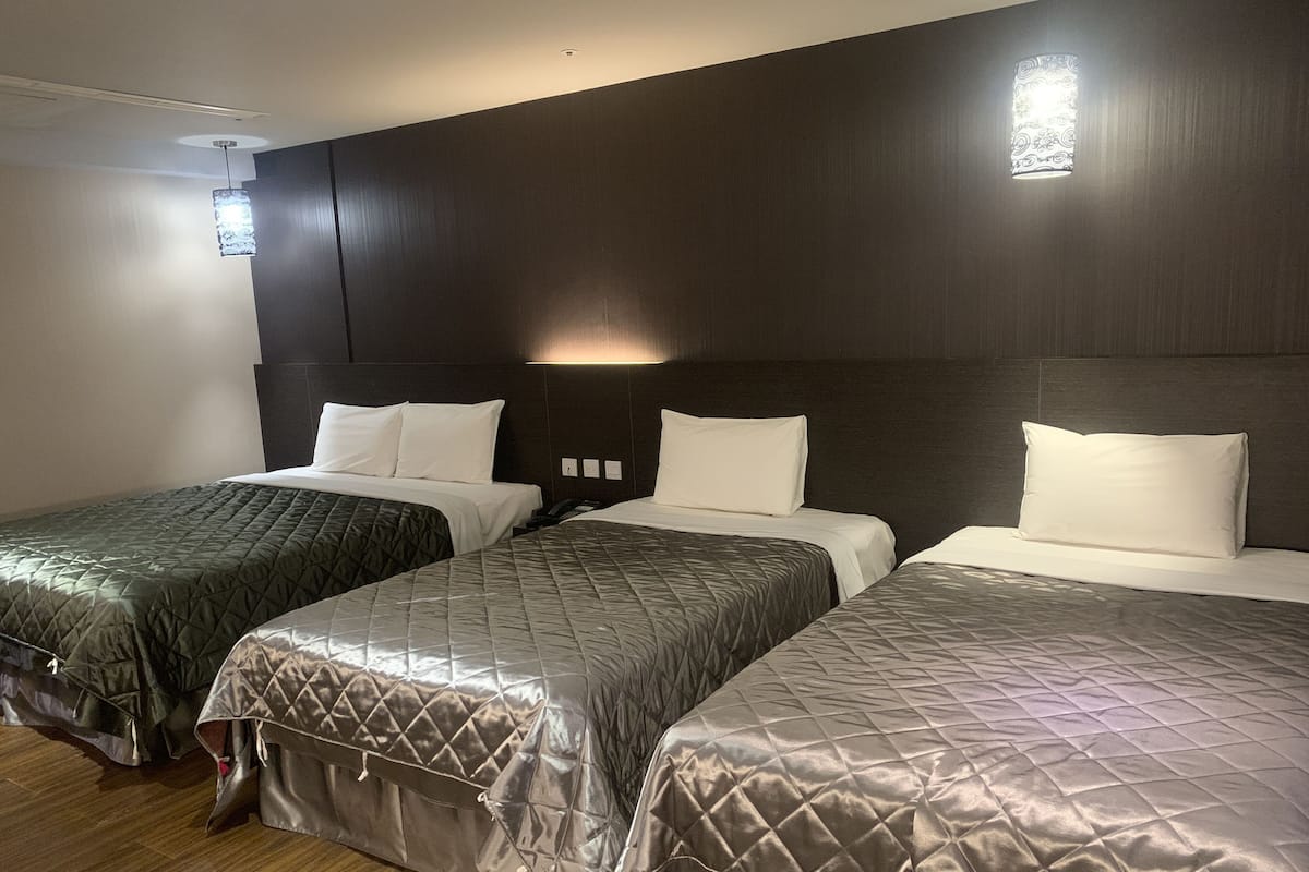 A hotel room with two beds, dark wooden headboards, and a small window with decorative glass.