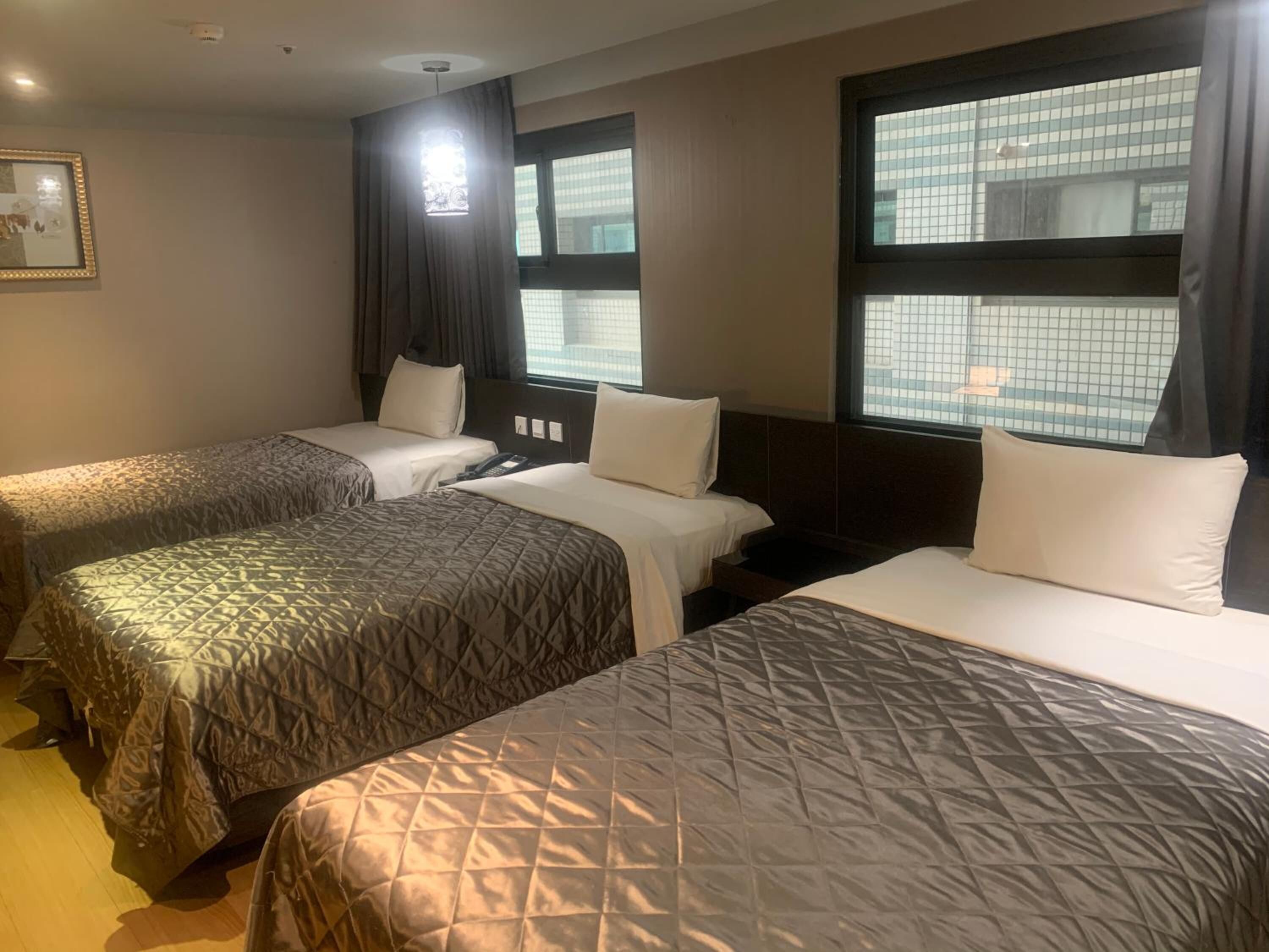 Hotelkamer met twee bedden, een nachtkastje, een telefoon en grote ramen met gordijnen.