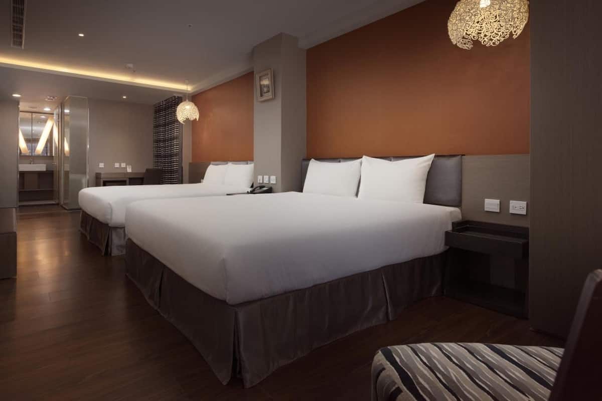 A hotel room with two beds, a small seating area, a desk, and a bathroom.