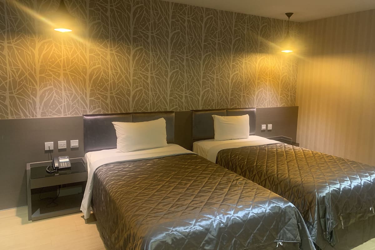 A hotel room with two beds, a nightstand with a phone, and a wall with a tree pattern.
