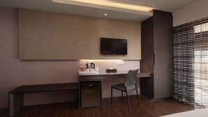 Una moderna camera d'albergo con una scrivania in legno, una sedia, una TV a schermo piatto montata a parete e un angolo cottura.
