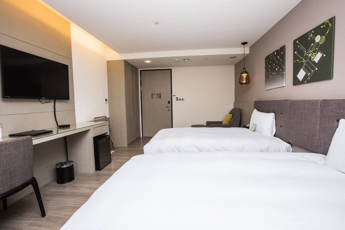 Une chambre d’hôtel avec deux lits, un bureau, une télévision et des œuvres d’art accrochées au mur.