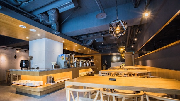 Un intérieur de restaurant moderne avec des tables et des chaises en bois, un bar central et un éclairage d’ambiance.