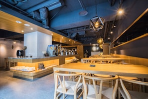 Un interior de restaurante moderno con mesas y sillas de madera, una zona de bar central e iluminación ambiental.
