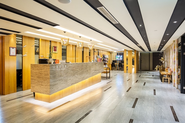 Una moderna recepción de hotel con mostrador de mármol, detalles de madera y un interior limpio y bien iluminado.