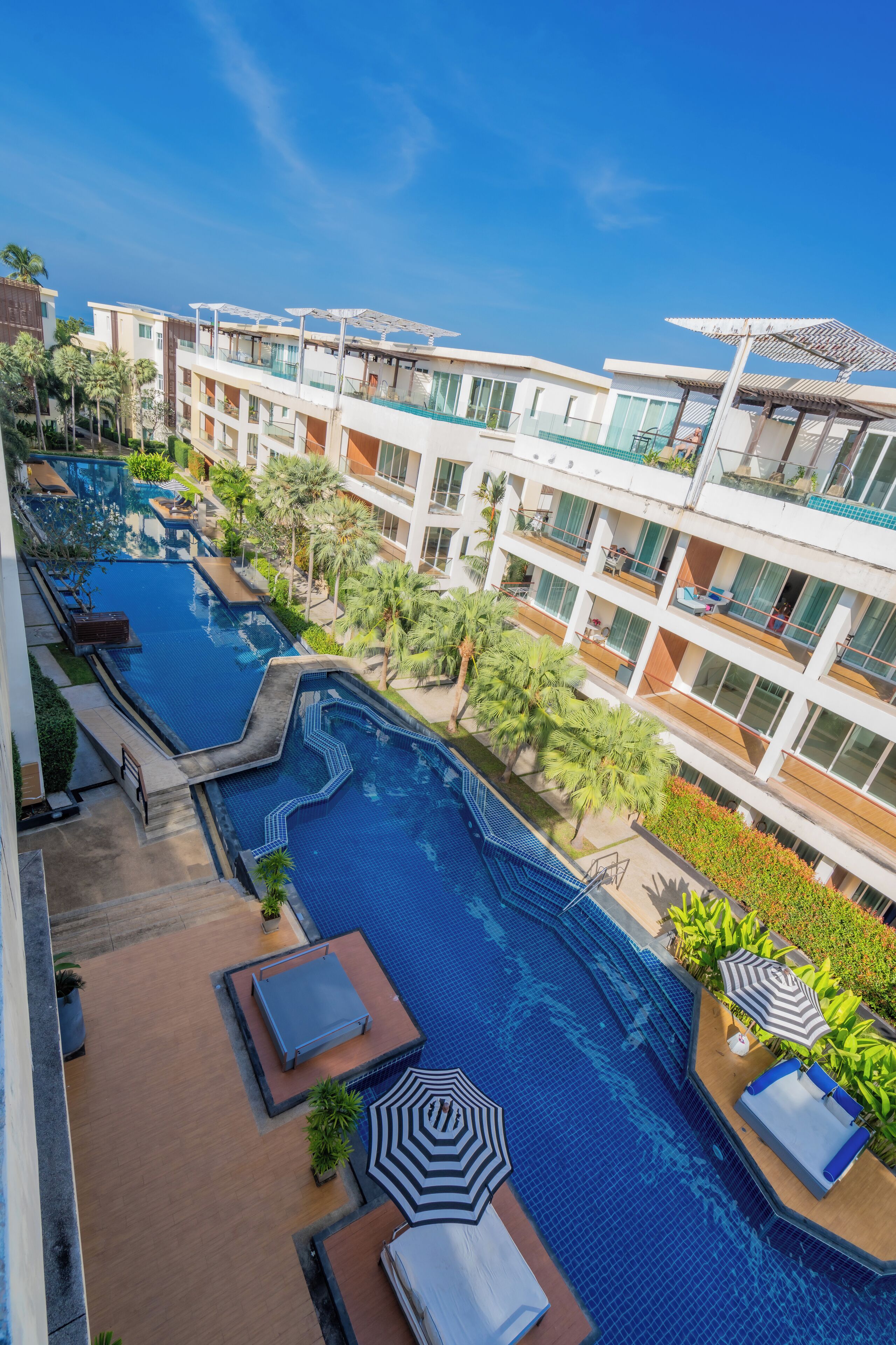 A hotel with multiple swimming pools, outdoor seating areas, and a modern architectural design.
