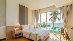 A modern hotel room with a large bed, bedside tables, a desk, and a view of the ocean through floor-to-ceiling windows. - The Pelican Residence & Suite Krabi (Krabi)