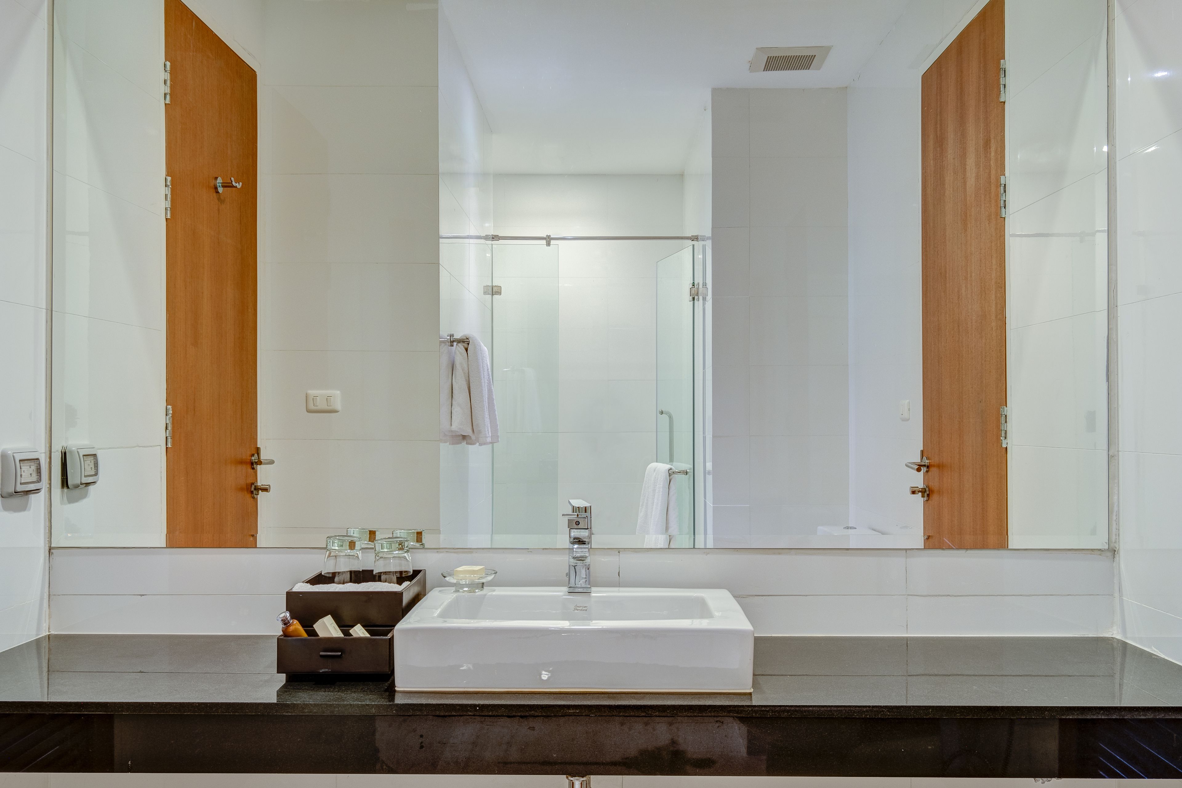 Un baño moderno con un espejo grande, un lavamanos rectangular y puertas de madera.