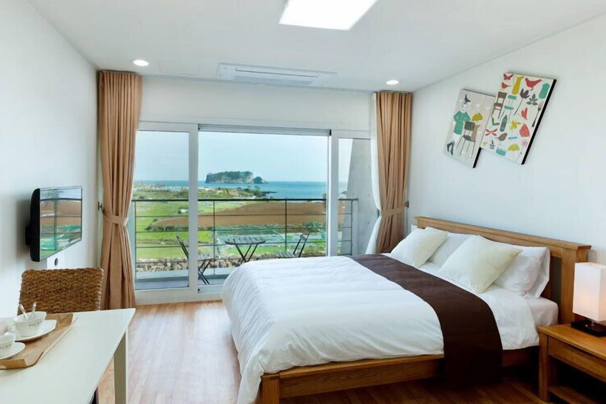 Een hotelkamer met een groot bed, een televisie, een eettafel met een dienblad vol bekers en een balkon met uitzicht op zee.