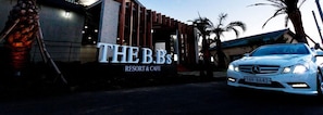 Un edificio con un letrero que dice "THE B&B RESORT & CAFE" y un coche blanco estacionado adelante.