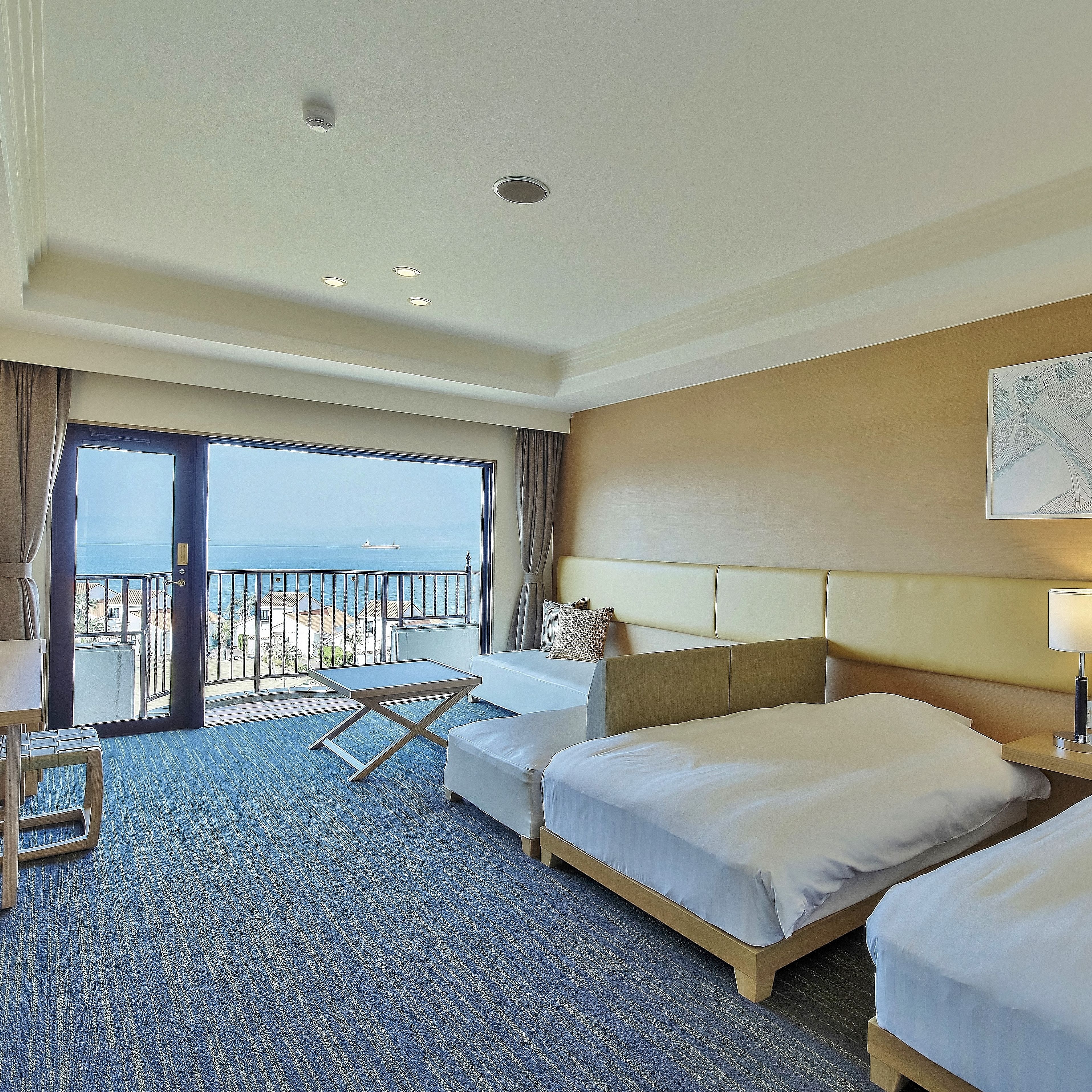 A hotel room with a large balcony, two beds, a desk, and a view of the sea.