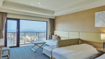 A hotel room with a large balcony, two beds, a desk, and a view of the sea.