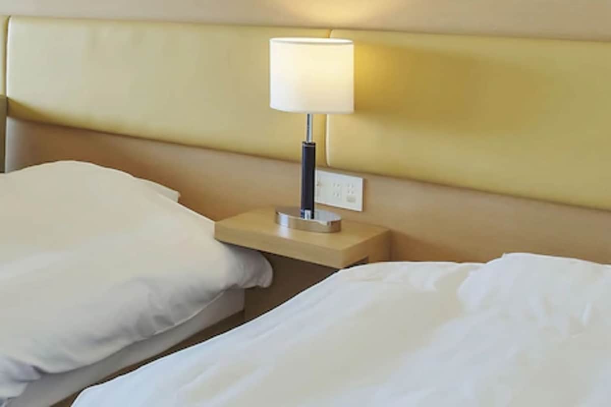 A hotel room with a bed, a nightstand with a lamp, and a wall-mounted artwork.