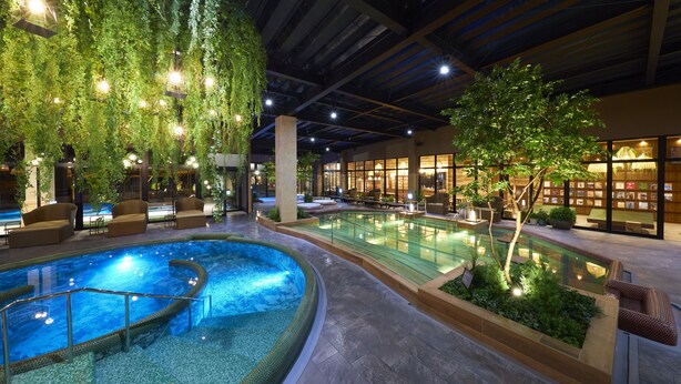 An indoor swimming pool with a glass barrier, surrounded by lounge areas and a restaurant with a view of the pool.
