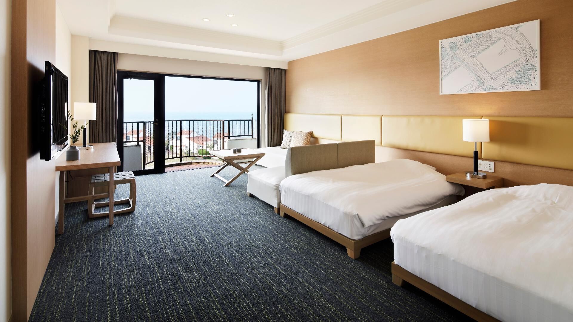 A hotel room with two beds, a desk, a chair, a TV, and a balcony with a view.