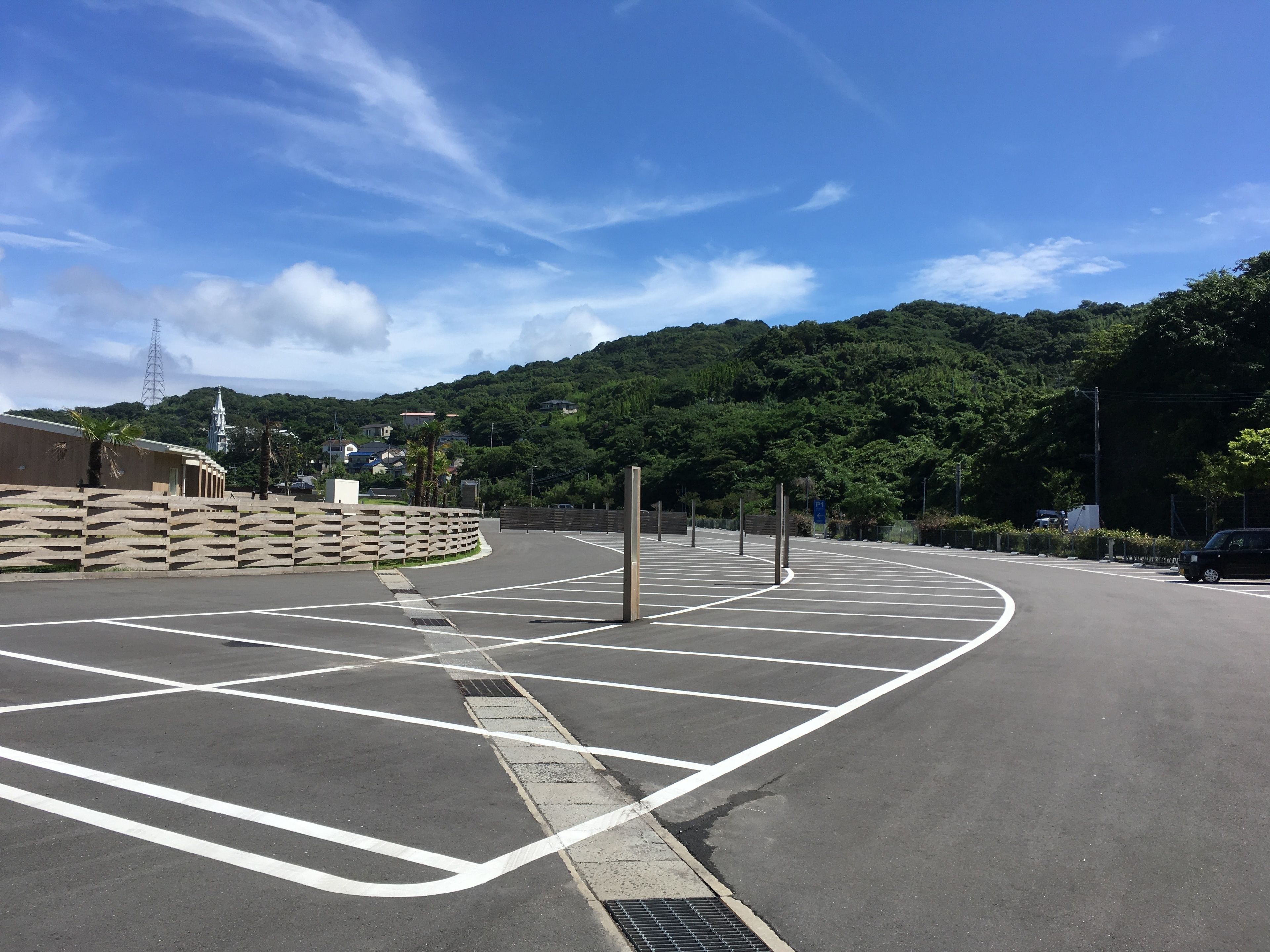 A parking lot with marked spaces and a curved road leading to a building with a fence.