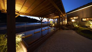 A covered outdoor area with a wooden structure, a paved walkway, and a view of a body of water in the background.