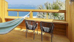 A wooden deck with two chairs and a hammock, overlooking a body of water and distant mountains.
