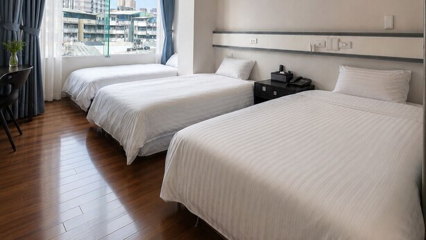 Een hotelkamer met twee bedden, een bureau en een groot raam met uitzicht op de stad.