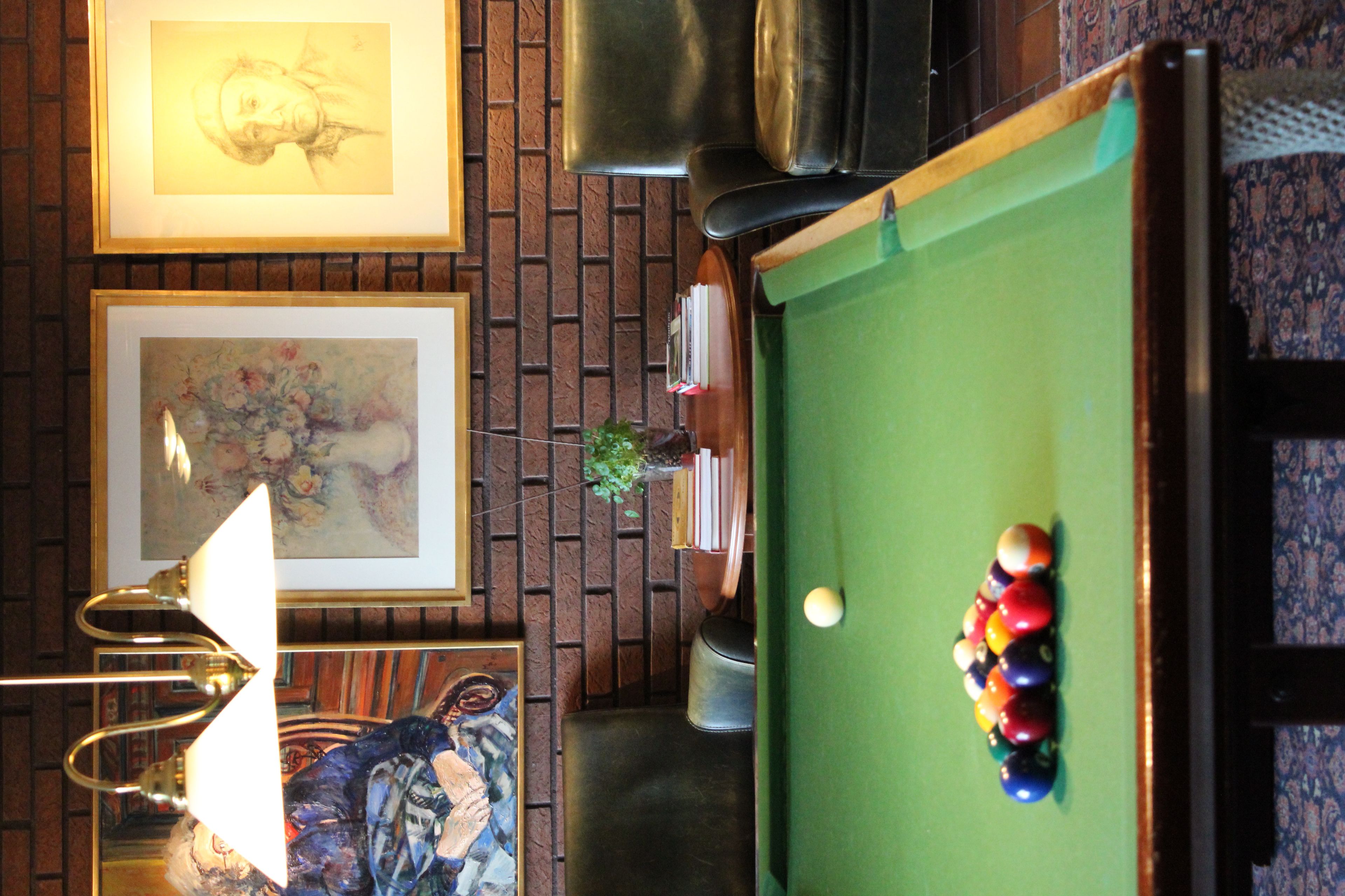 A billiards table with balls, a framed painting, a lamp, and a brick wall.