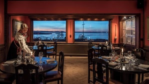 Een restaurant met gedekte tafels, uitzicht op een zonsondergang over het water, en een ober die een tafel bedient.