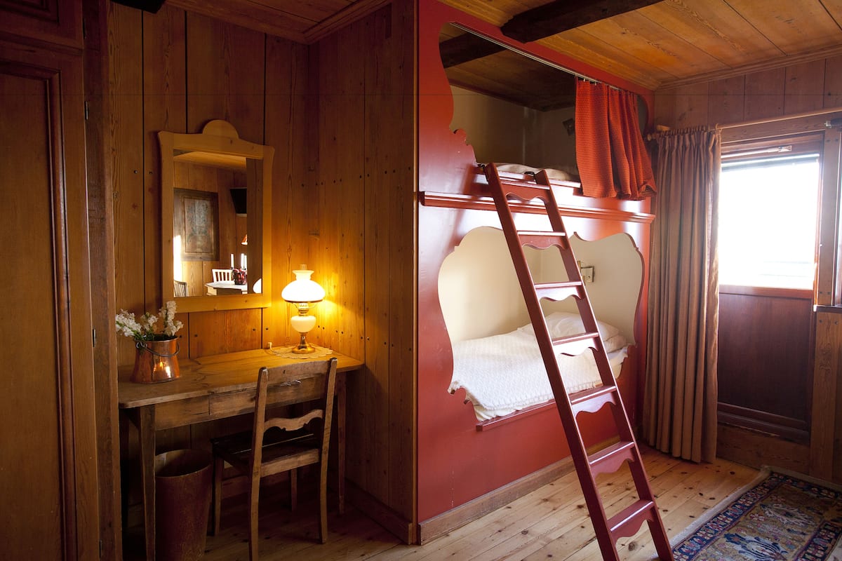 Una habitación de madera con una cama litera, un escritorio con lámpara y una silla.