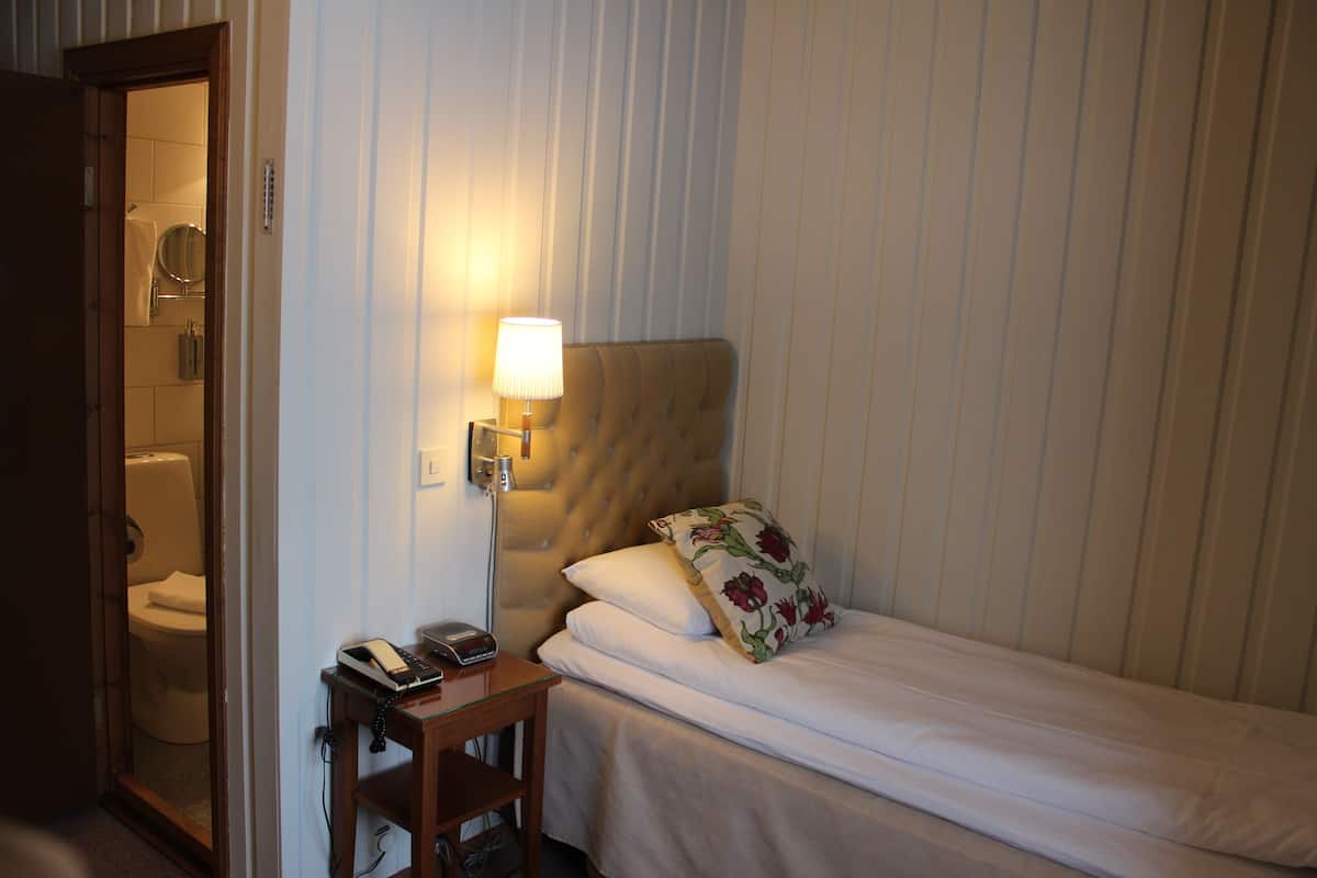 Una habitación de hotel con una cama, una mesita de noche con lámpara, un teléfono y un espejo.