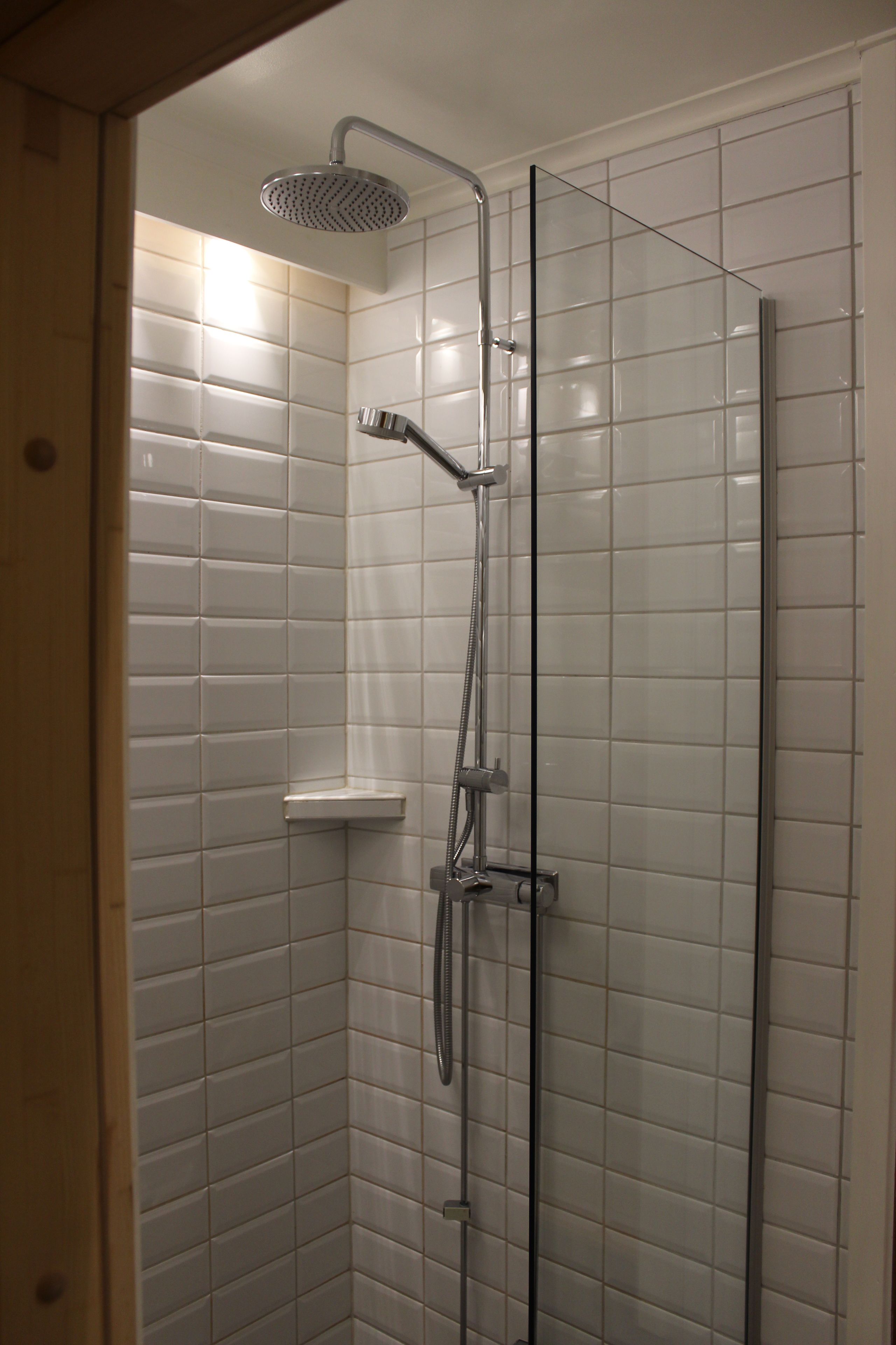 A shower with a glass door, chrome fixtures, and white tiled walls.