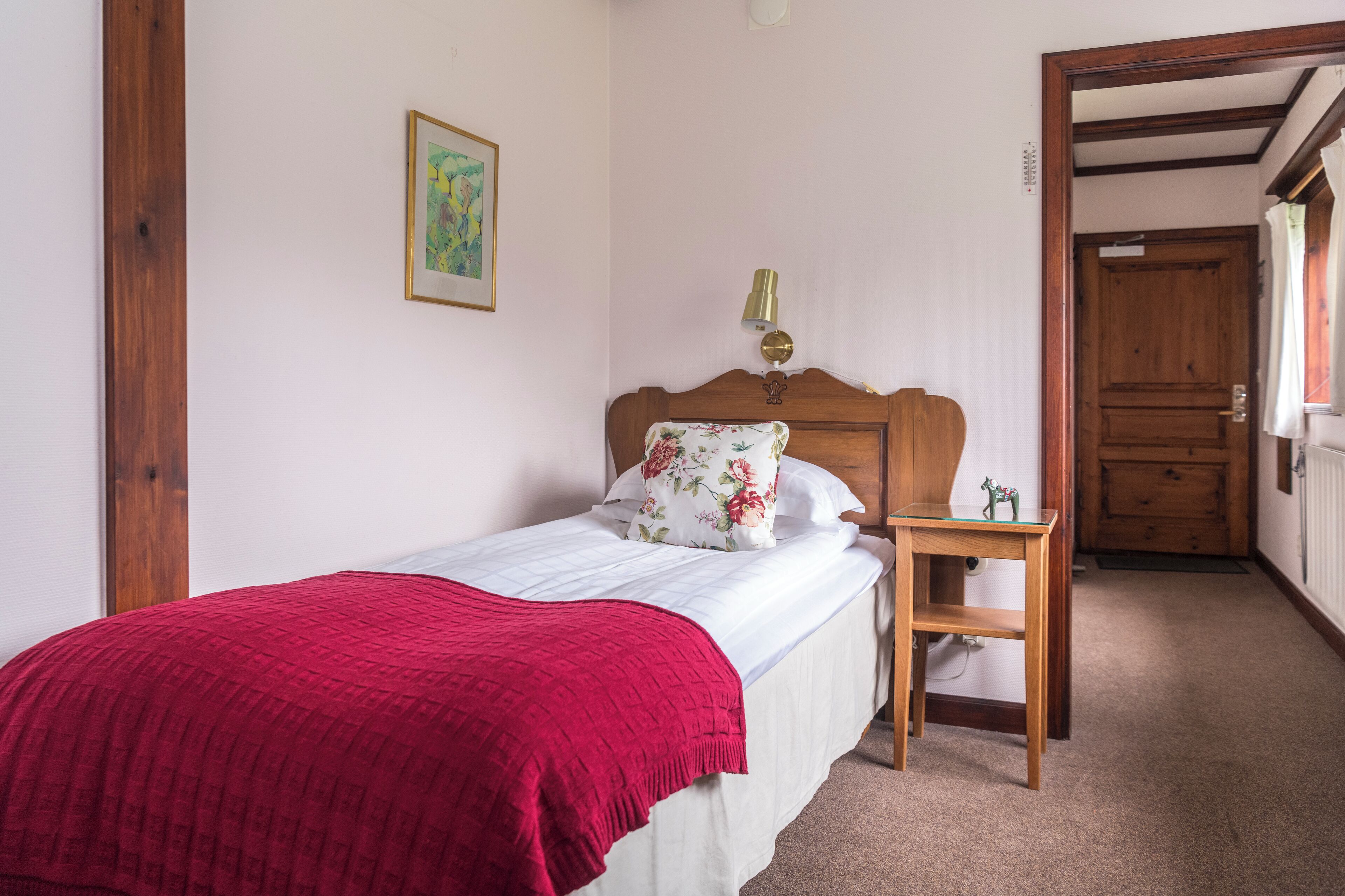 A bedroom with a single bed, a nightstand, a lamp, and a door leading to another room.