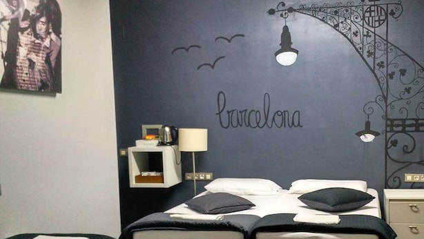 A bedroom with two beds, a wall-mounted lamp, a small shelf with a kettle, and a wall decoration with the word "Barcelona". - Don Moustache Hostel (Barcelona)