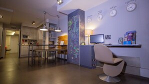 A modern kitchen with a dining area, a computer desk, and a chair. There are clocks on the wall and a sign with a name. - Don Moustache Hostel (Barcelona)