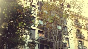 A multi-story building with balconies, a tree in front, and a storefront with a motorcycle parked outside. - Don Moustache Hostel (Barcelona)