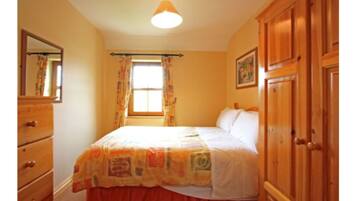 A bedroom with a bed, wooden wardrobe, a dresser, a window with curtains, and a ceiling light.