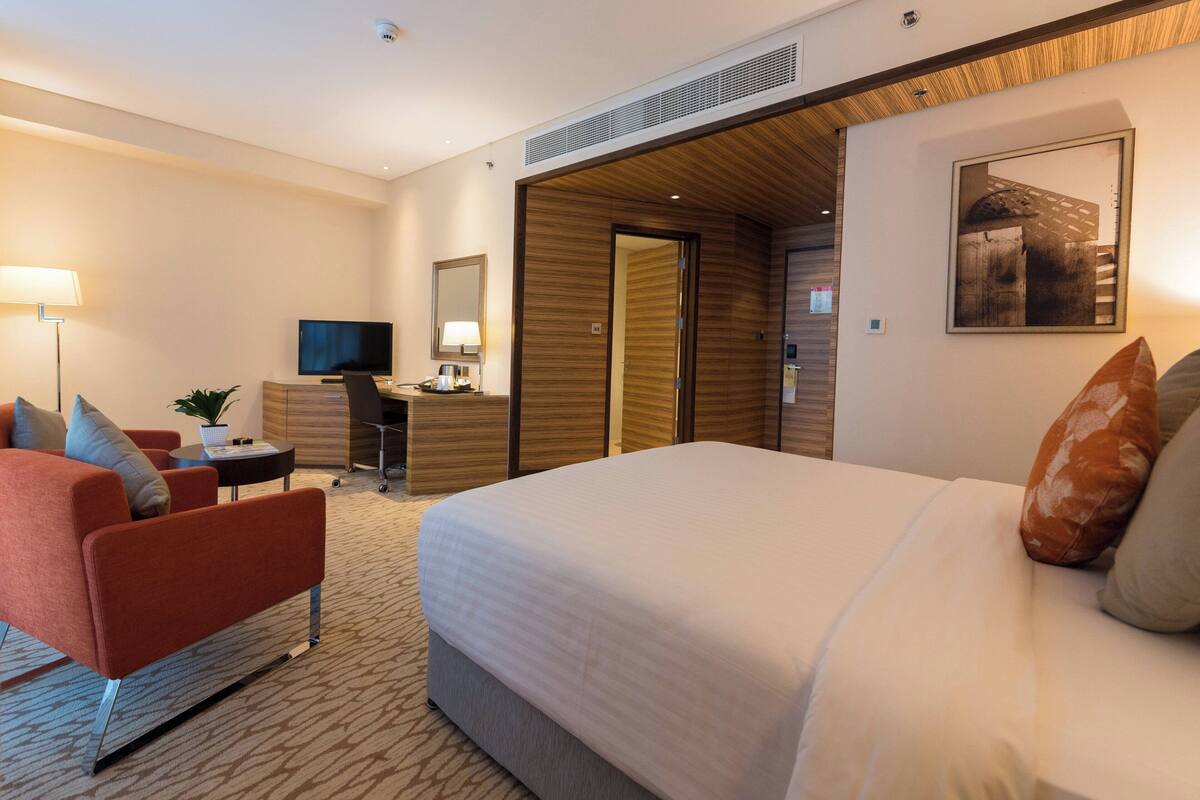 Ein Hotelzimmer mit einem großen Bett, einem Schreibtisch mit Stuhl, einem Fernseher und einer Lampe.