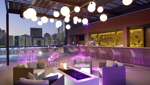 A rooftop bar with modern seating, a bar area with bottles, and a city view. - Courtyard by Marriott World Trade Center Abu Dhabi (Abu Dhabi)
