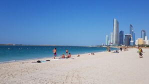 A beach with people sunbathing and swimming, and a city skyline with modern buildings in the background. - Courtyard by Marriott World Trade Center Abu Dhabi (Abu Dhabi)