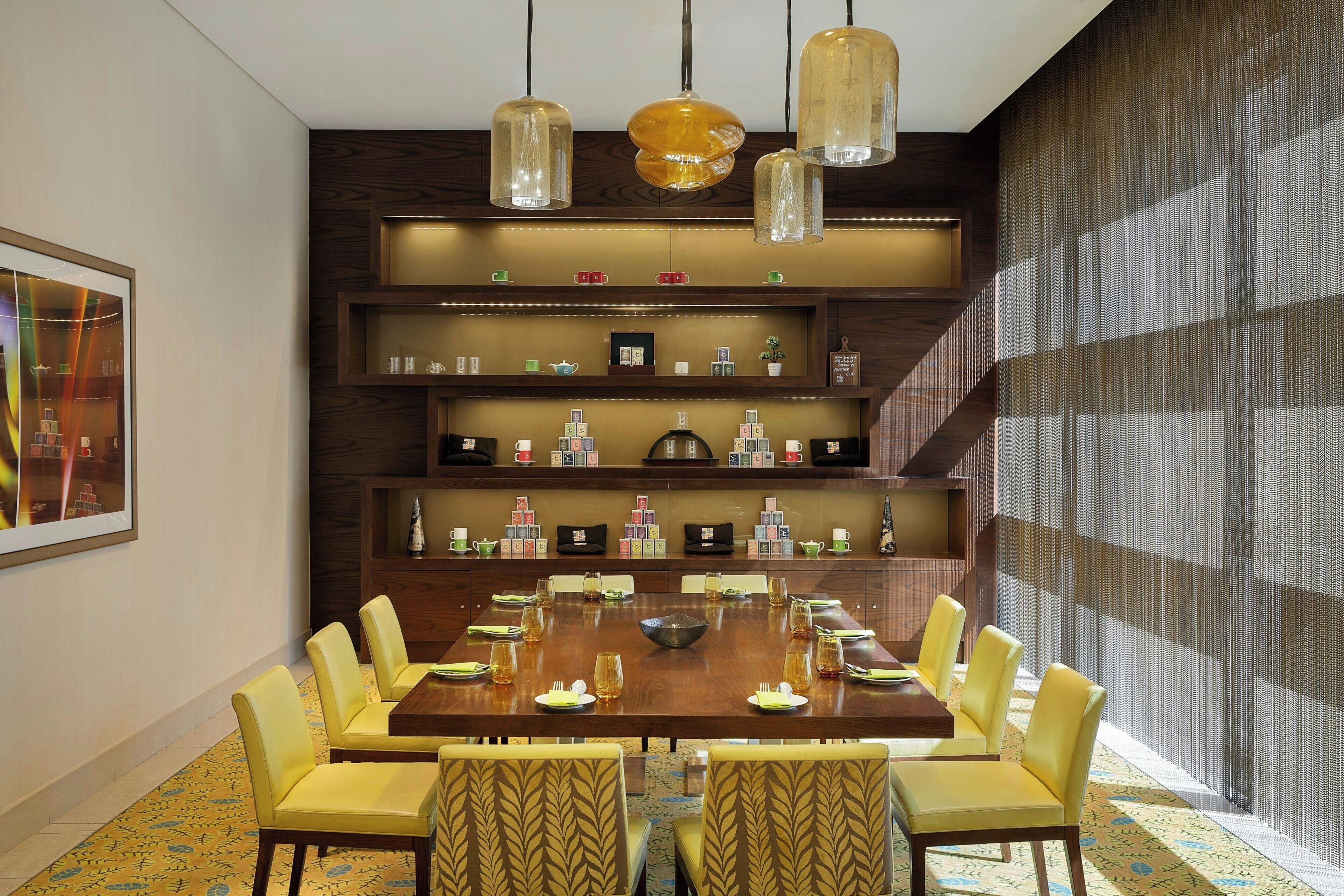 A dining area with a large wooden table, yellow chairs, and hanging pendant lights.