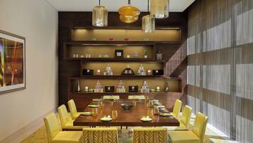 Un comedor con una gran mesa de madera, sillas amarillas y lámparas colgantes.