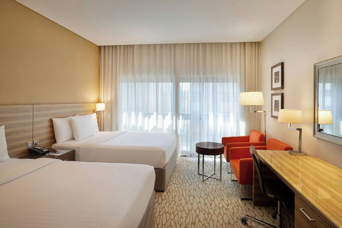 Ein Hotelzimmer mit zwei Betten, einem Schreibtisch, einem Stuhl und einem kleinen Tisch.