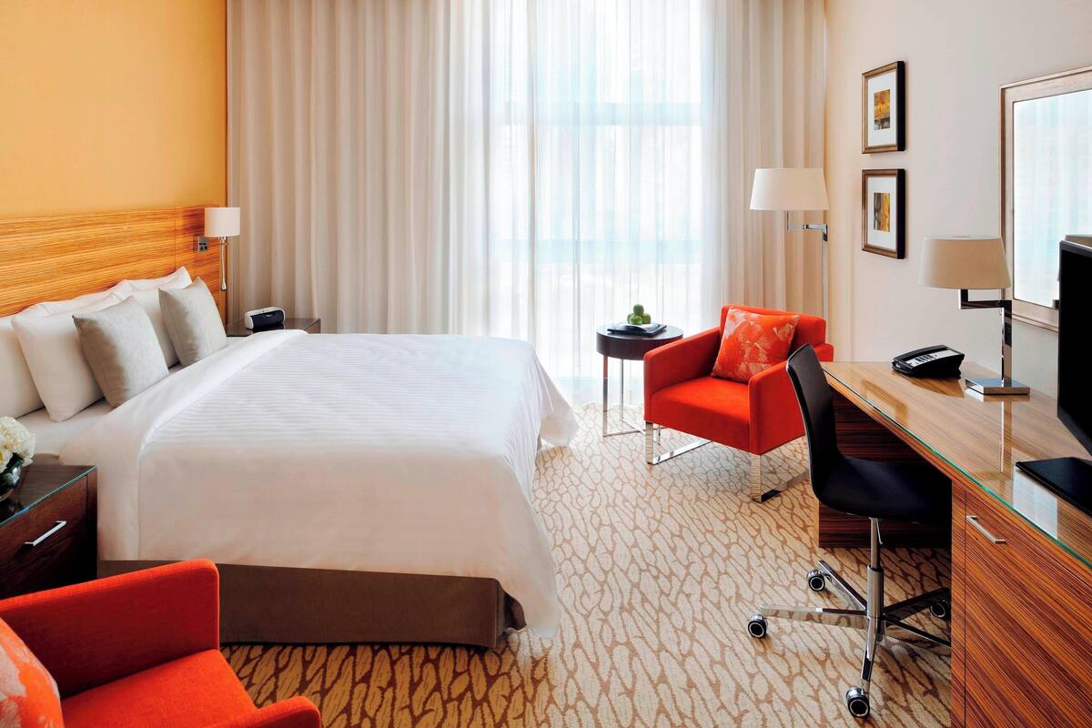 Ein Hotelzimmer mit einem großen Bett, einem Schreibtisch mit Computer, einem Sessel und einem Fernseher.
